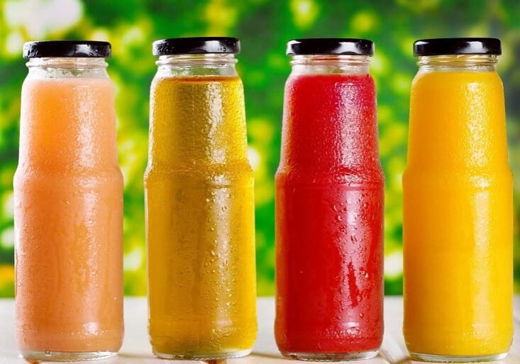 A row of different colored drinks in glass bottles.