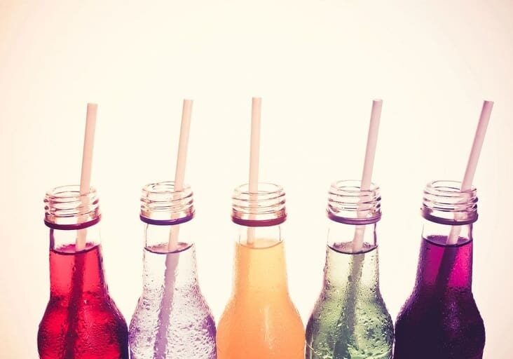 A row of soda bottles with straws in them.