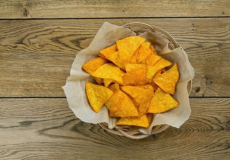 A basket of tortilla chips on top of a wooden table.